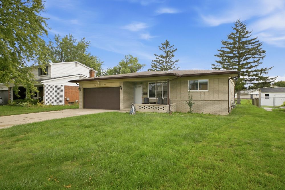 Ranch-style home with attached garage, manicured lawn, and mature trees on a sunny day.