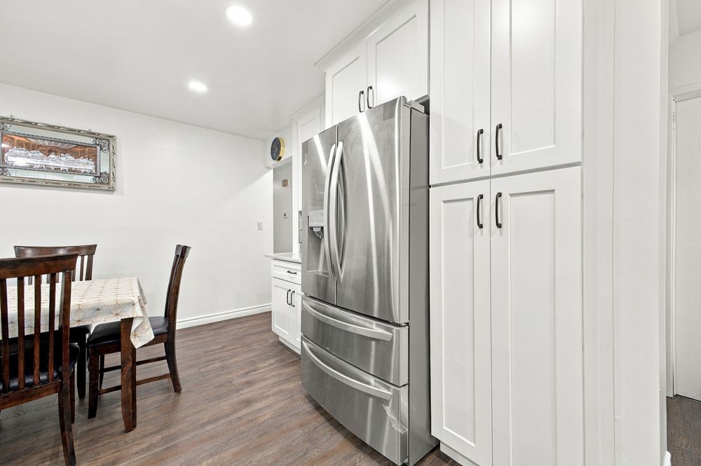 Modern kitchen with stainless steel French door refrigerator, white shaker cabinets, and dark hardwood floors.
