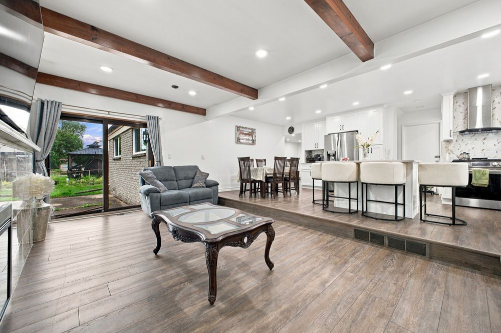 Open-concept living room with wood beam ceilings, hardwood floors, glass coffee table, and modern kitchen with bar seating.