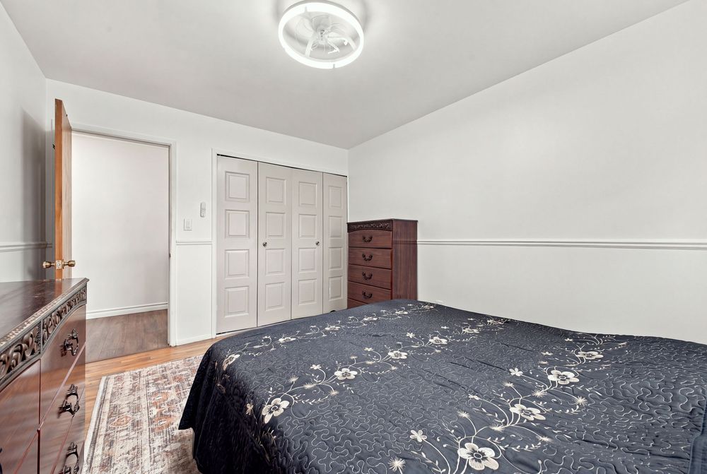 Cozy bedroom with a dark floral bedspread, hardwood floors, white closet doors, and a wooden dresser.