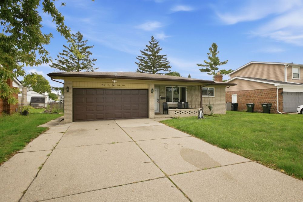 Ranch-style home with attached garage, manicured lawn, concrete driveway, and mature evergreen trees in a suburban neighborhood.
