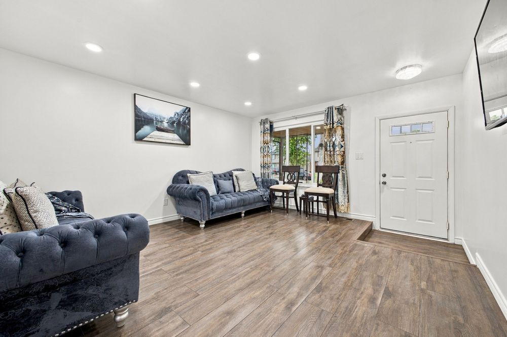 Bright living room with blue tufted sofas, hardwood floors, recessed lighting, and a white front door.