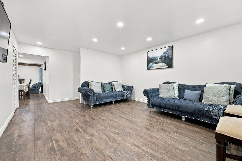 Spacious living room with hardwood floors, two blue velvet sofas, recessed lighting, and white walls.