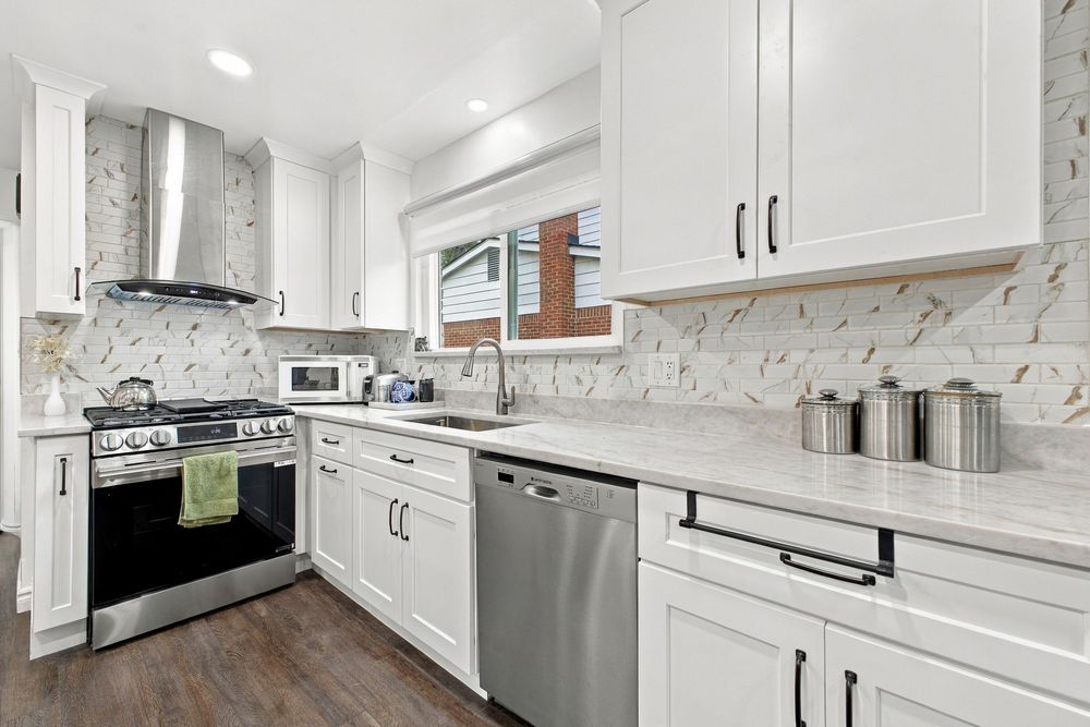 Modern white kitchen with quartz countertops, stainless steel appliances, marble backsplash, and dark hardwood floors.