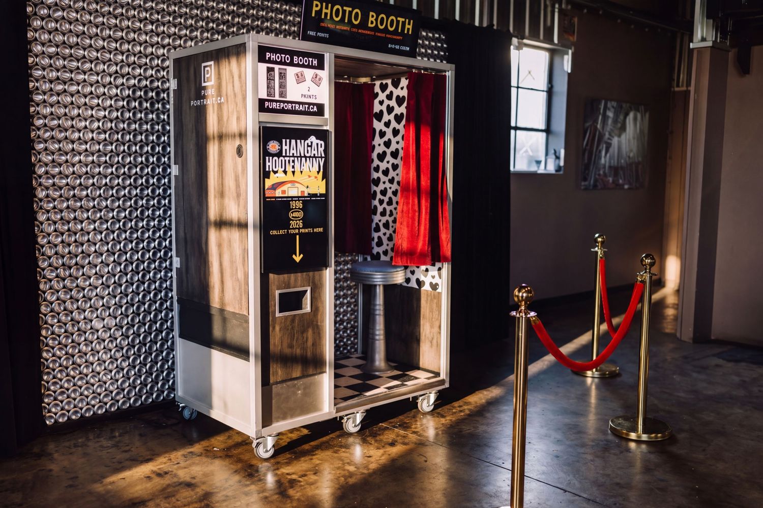 Vintage photo booth with red curtain and velvet rope barriers on a polished concrete floor at an event venue.