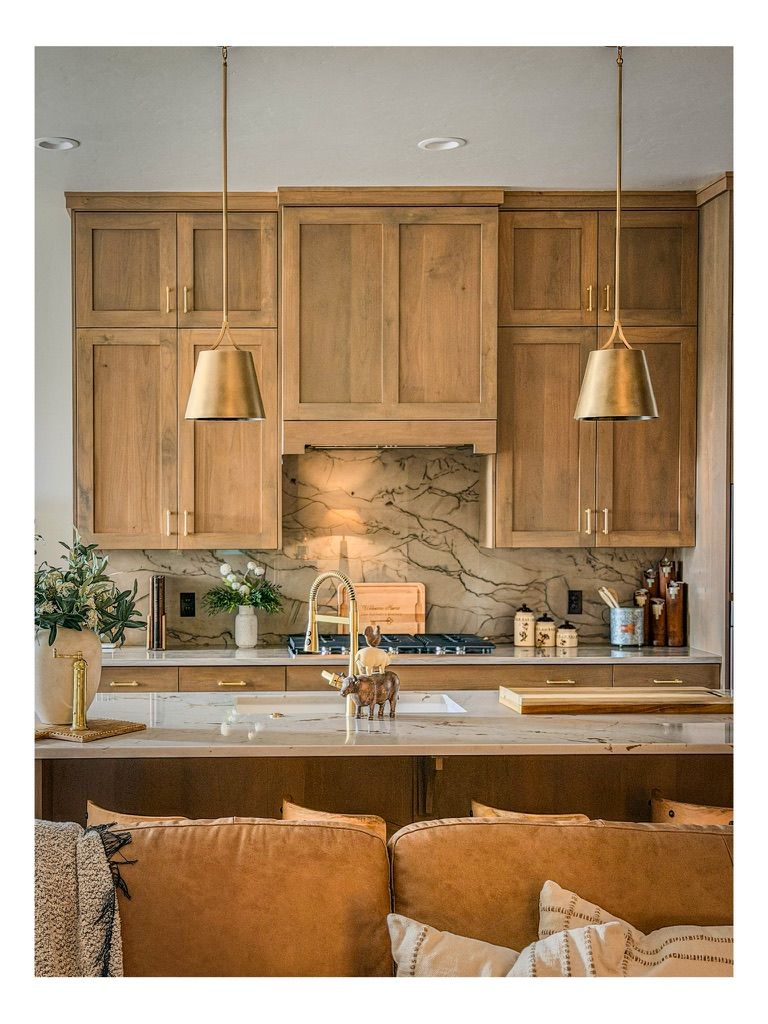 Warm wood kitchen cabinets with marble backsplash, gold pendant lights, and leather bar stools.