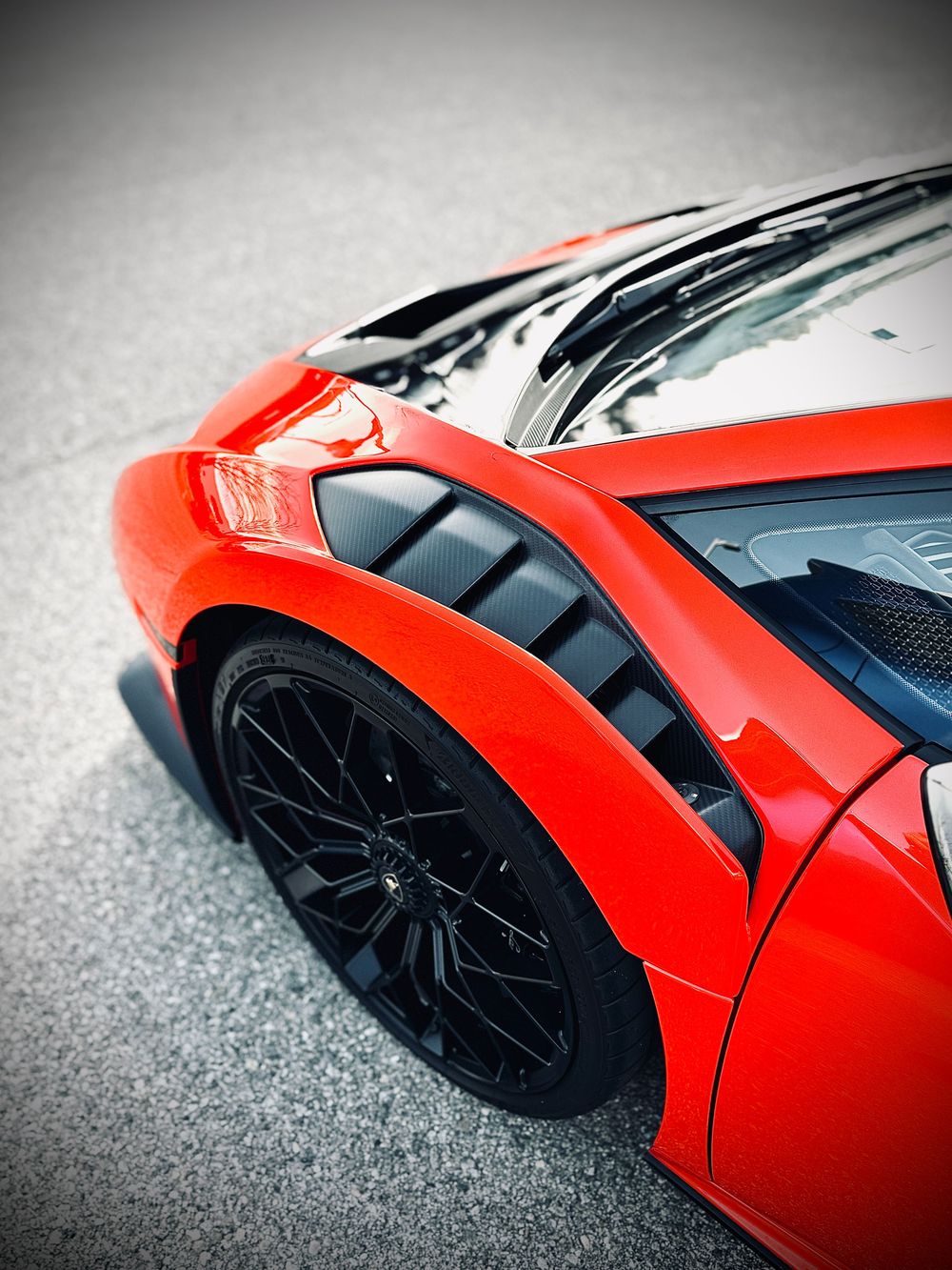 Red Lamborghini supercar detail shot showing black wheel and aerodynamic body panel.