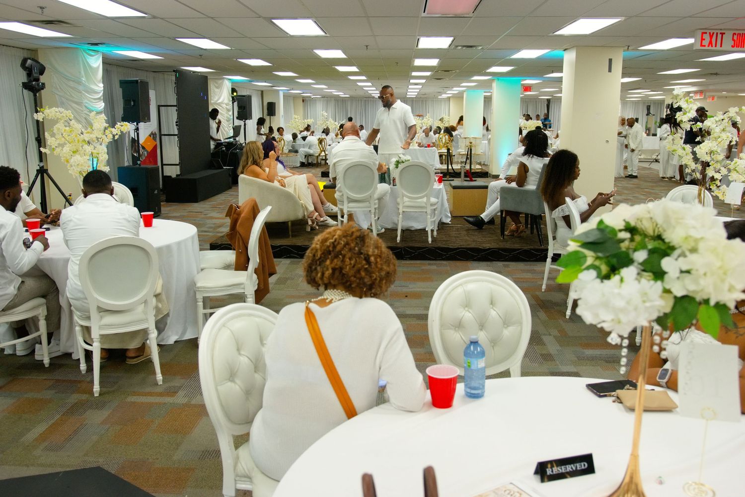 Elegant all-white indoor banquet event with guests dressed in white seated at decorated tables in a spacious venue.