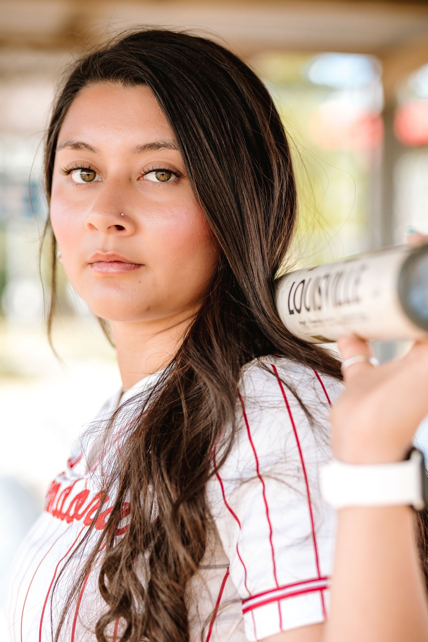 Young female softball player holding a Louisville Slugger bat over her shoulder in a white pinstripe jersey.