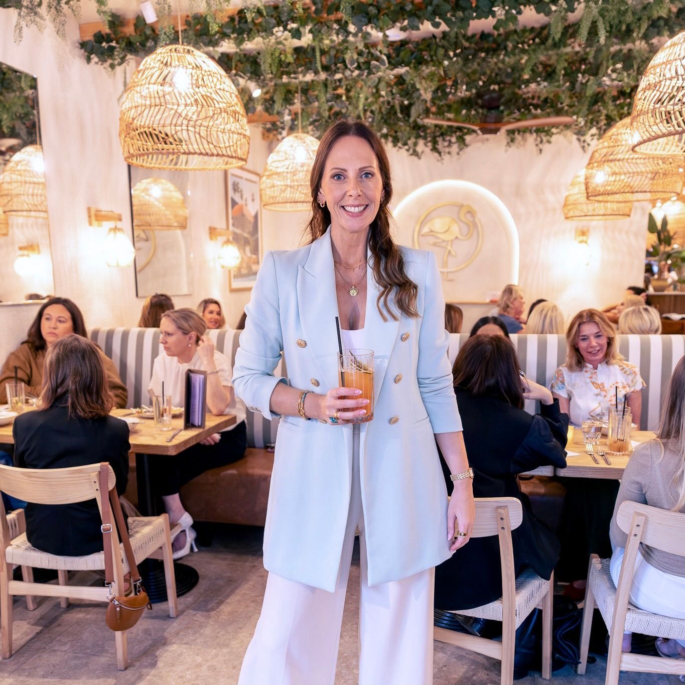 Smiling woman with long brown hair sitting at a decorated dining table with blue placemats and floral tableware indoors.