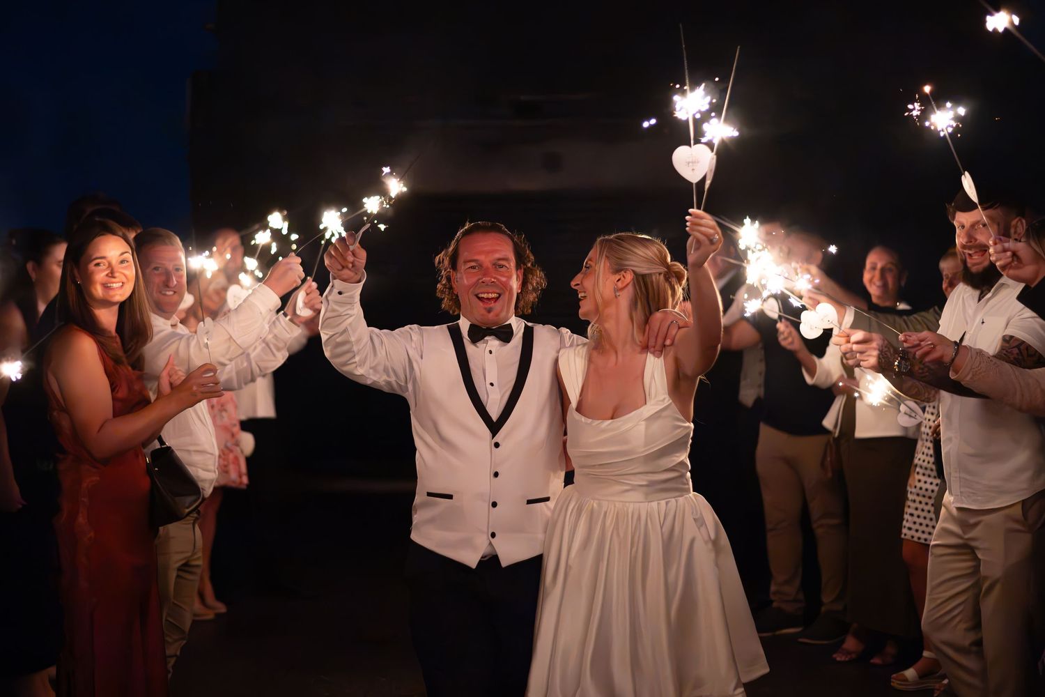 Bride and groom walk through sparkler send-off surrounded by cheering wedding guests at night. Wedding day, Sparklers. Leeds wedding UK