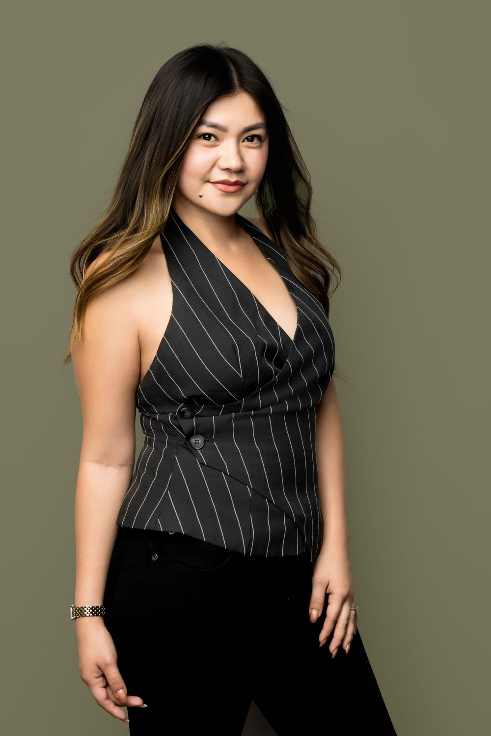 Young woman in black pinstripe halter vest and black pants posing confidently against an olive green background.