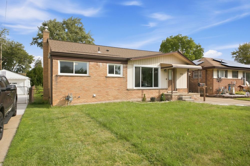 Brick ranch-style home with well-maintained lawn, large windows, and mature trees in a suburban neighborhood.