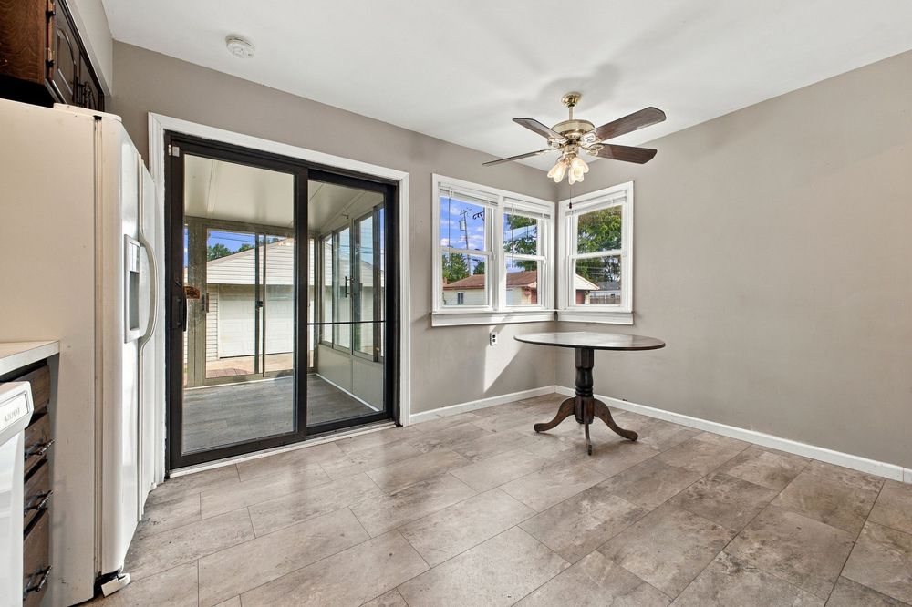 Bright dining area with tile floors, ceiling fan, sliding glass door to patio, and a small accent table by the window.