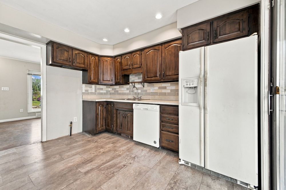 Kitchen with dark wood cabinets, white appliances, tile backsplash, and light hardwood floors.