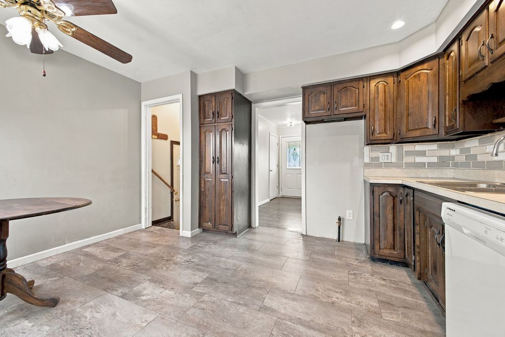 Dark wood kitchen cabinets with tile backsplash, white dishwasher, and hardwood floors in a spacious open layout.