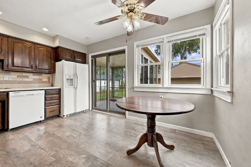 Bright kitchen and dining area with dark wood cabinets, white appliances, round table, ceiling fan, and sliding glass door.