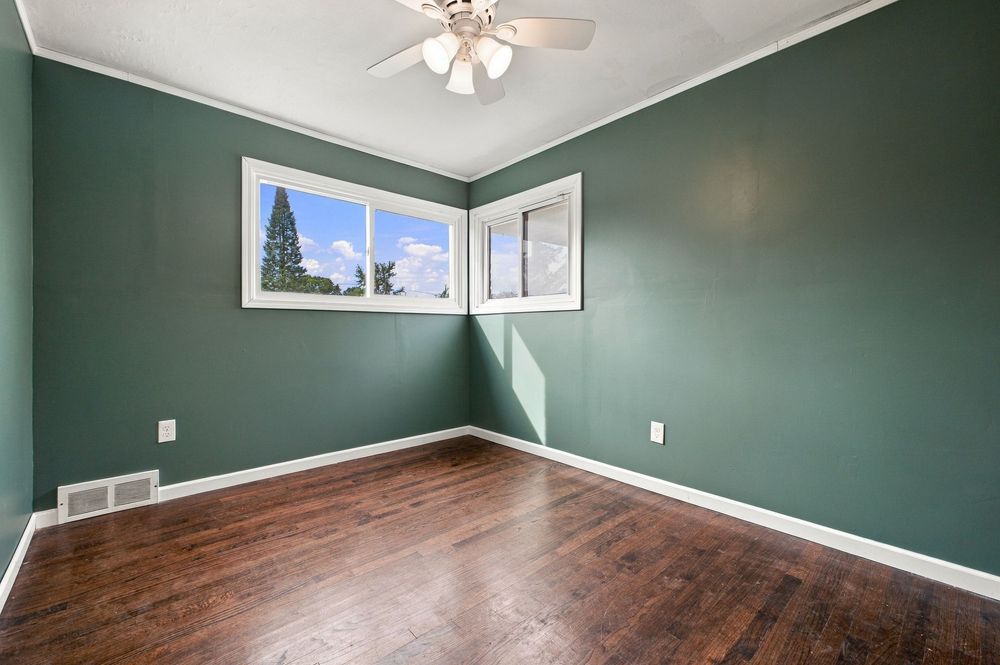 Empty room with green walls, hardwood floors, ceiling fan, and a window with natural light.