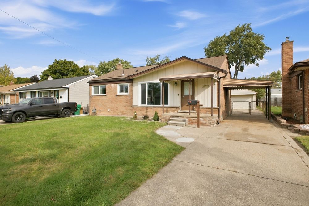 Brick ranch-style home with attached carport, manicured lawn, and mature trees on a sunny day.
