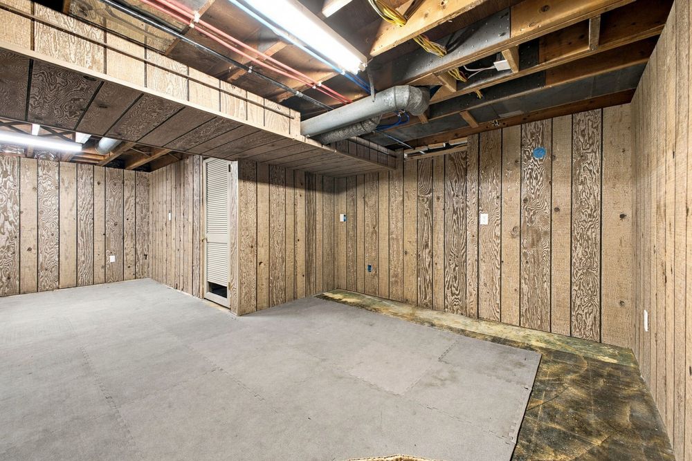 Unfinished basement with wood-paneled walls, exposed ceiling beams, ductwork, and concrete floor offering ample storage space.