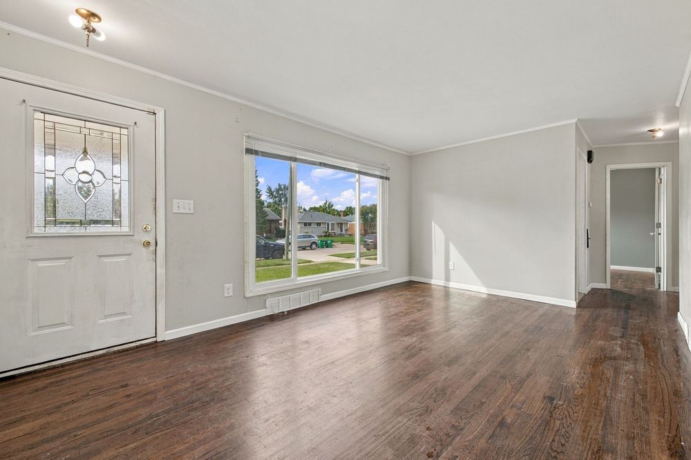 Bright entryway with hardwood floors, white front door with decorative glass, crown molding, and large window with natural light.