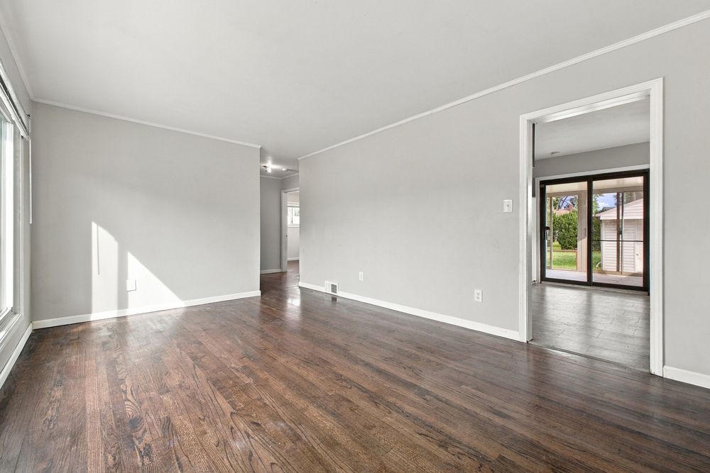 Bright empty living room with dark hardwood floors, white walls, crown molding, and sliding glass doors leading to outdoor space.