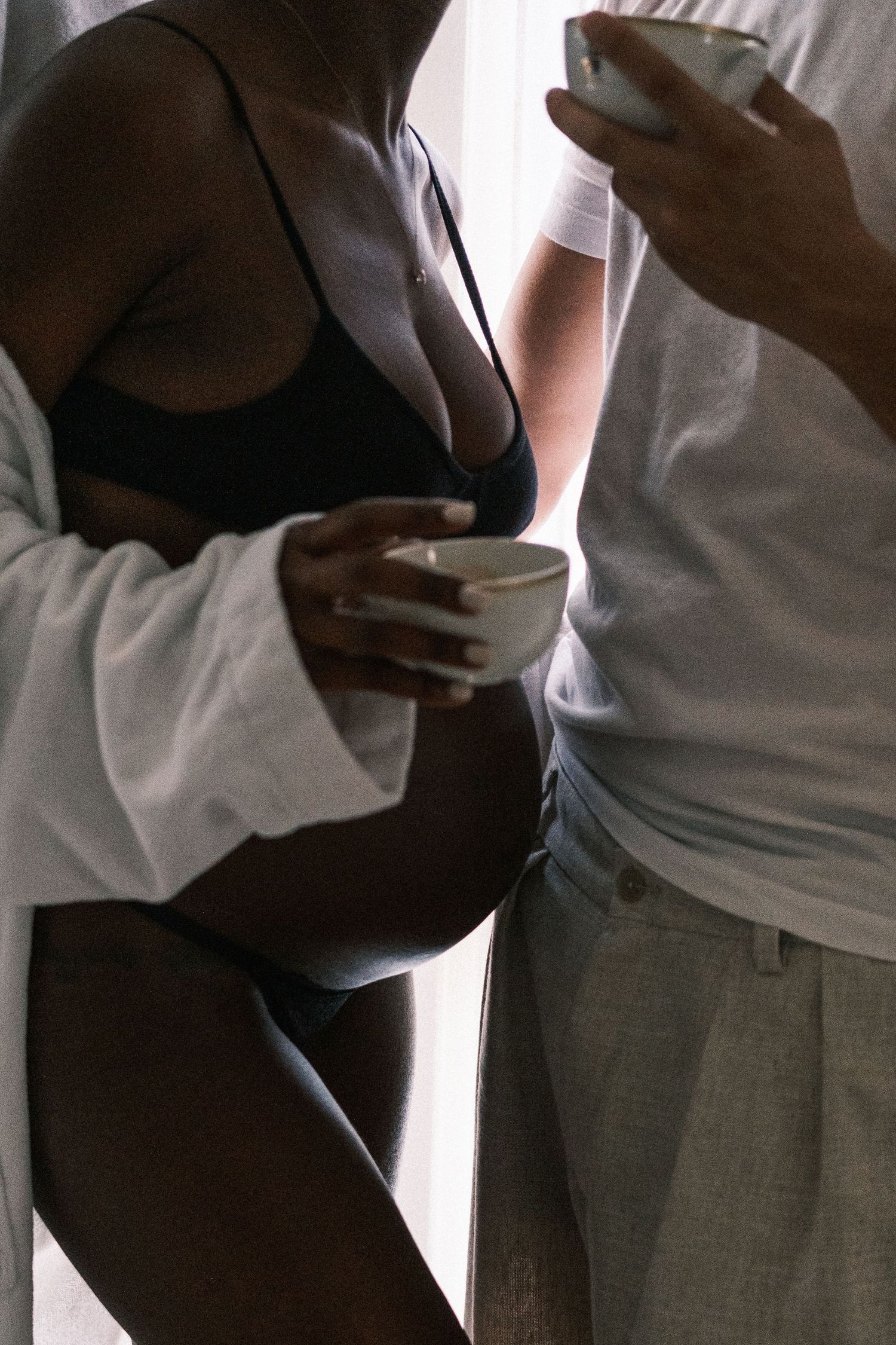 A pregnant woman in a white shirt receives a tender kiss from her partner while sitting together at a dark round table.