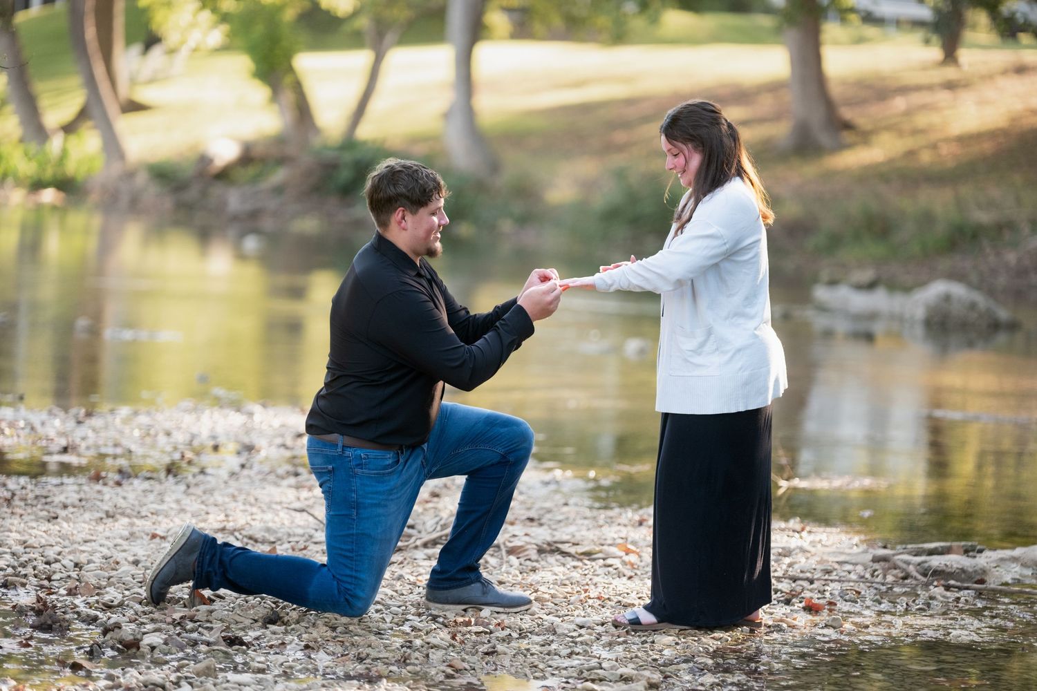 Man proposing marriage on one knee to woman by a peaceful riverside in Salado Texas Creek
