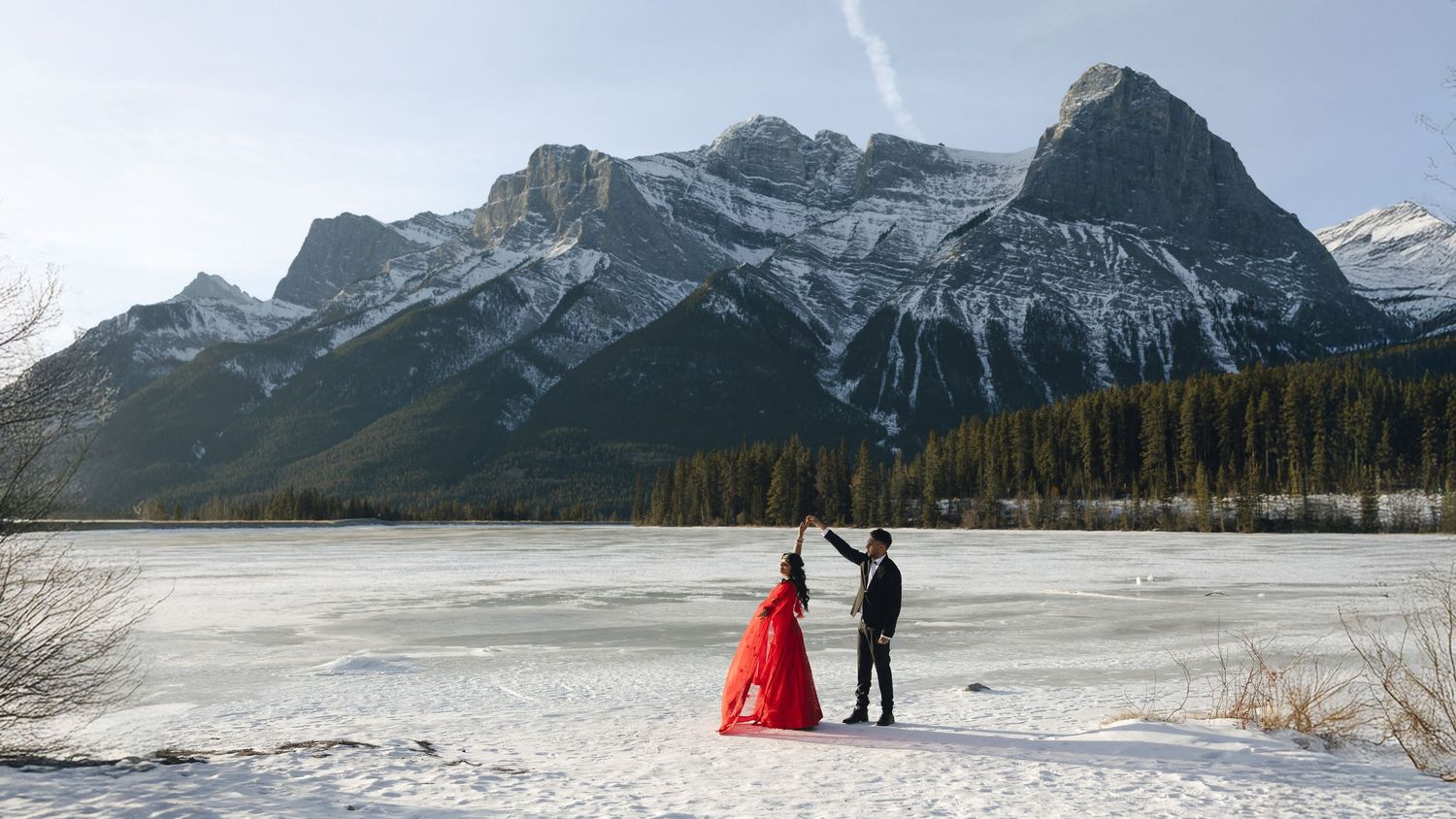 A snowy winter scene at the base of mountain peaks in Canmore with a flowing red dress against the icy landscape.