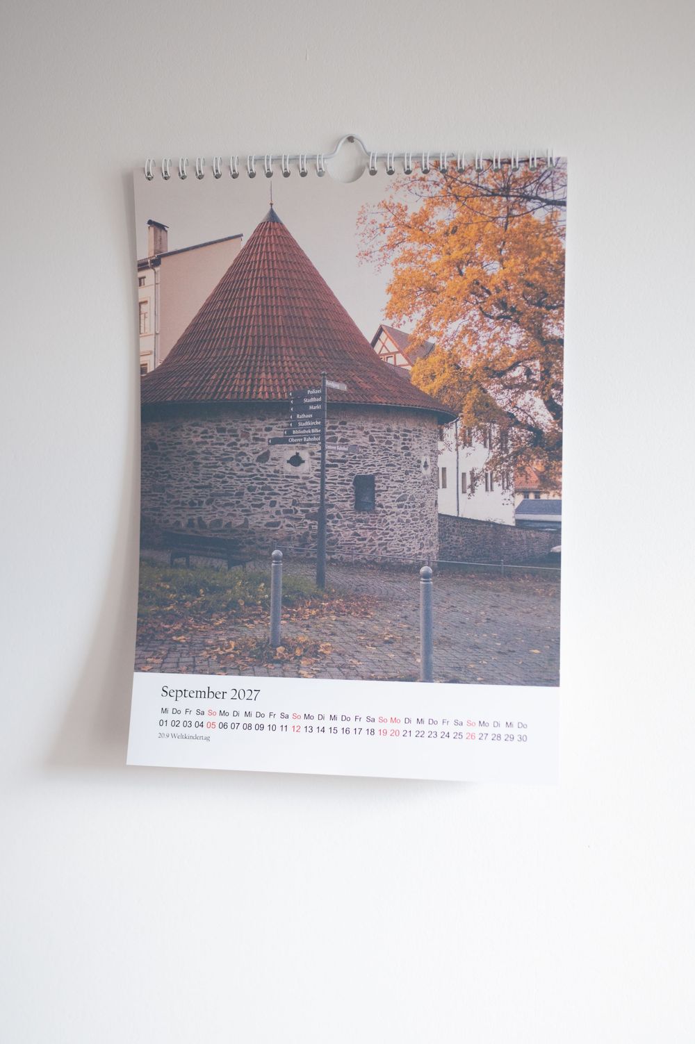 September 2027 wall calendar featuring a stone tower with red roof and autumn trees in a European town.
