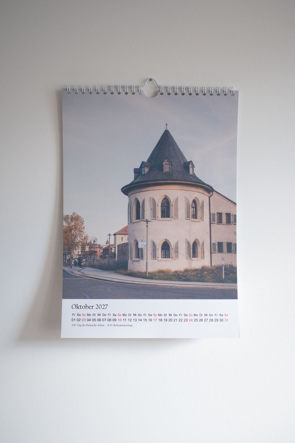 Wall calendar showing October 2027 with a photo of a historic round tower building on a European street.