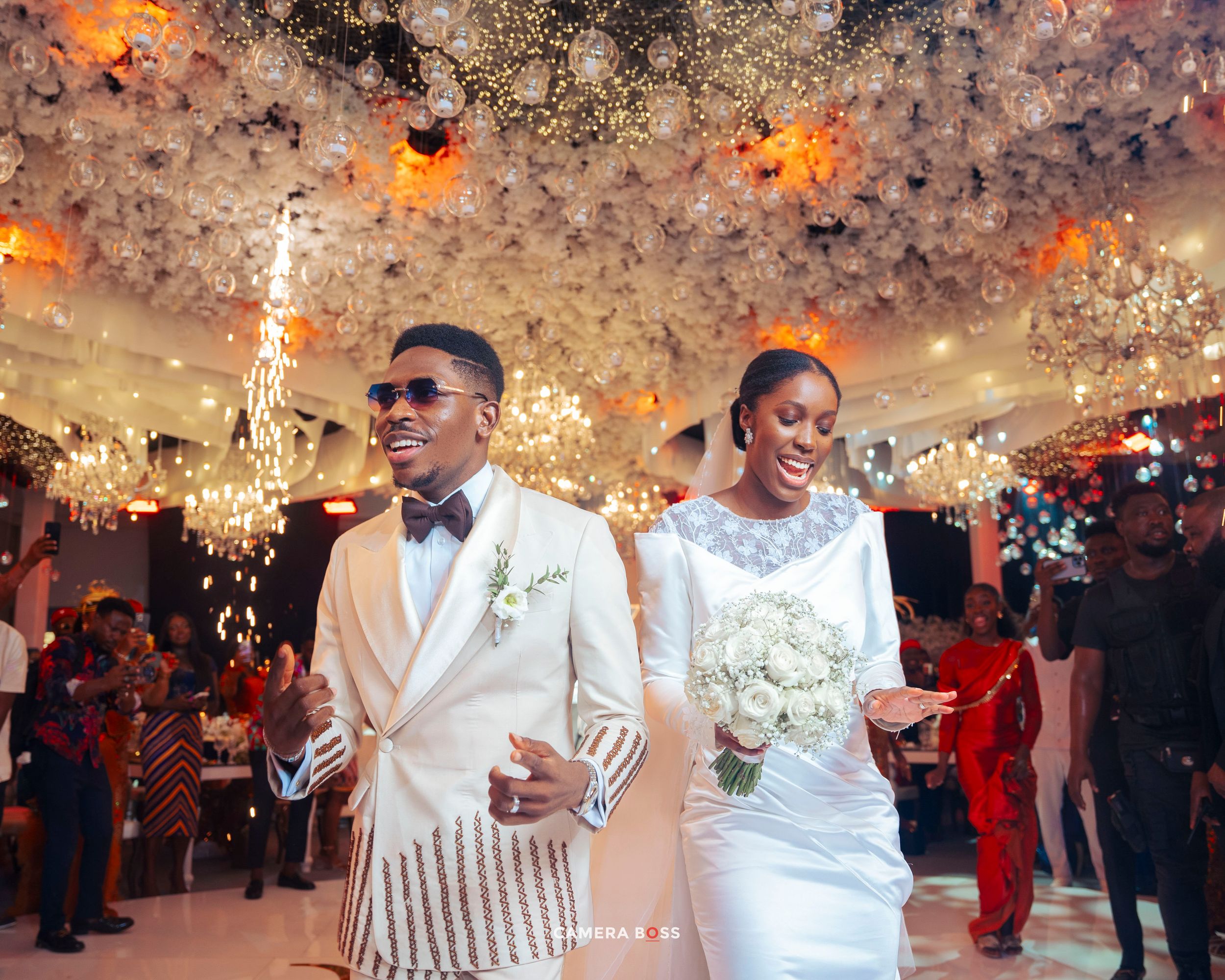 A couple celebrates at their wedding reception under an ornate ceiling with twinkling lights and confetti during their first dance.