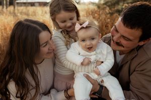 Happy family of four with two young daughters sharing a warm embrace outdoors in a golden field.