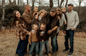 Large family group photo outdoors in winter, smiling together among bare trees in casual fall clothing.