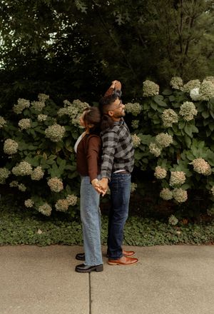 A couple holds hands and dances outdoors in front of lush green hydrangea bushes in full bloom.