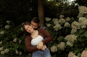 Couple embracing among blooming hydrangeas in a lush garden, sharing a romantic moment outdoors.