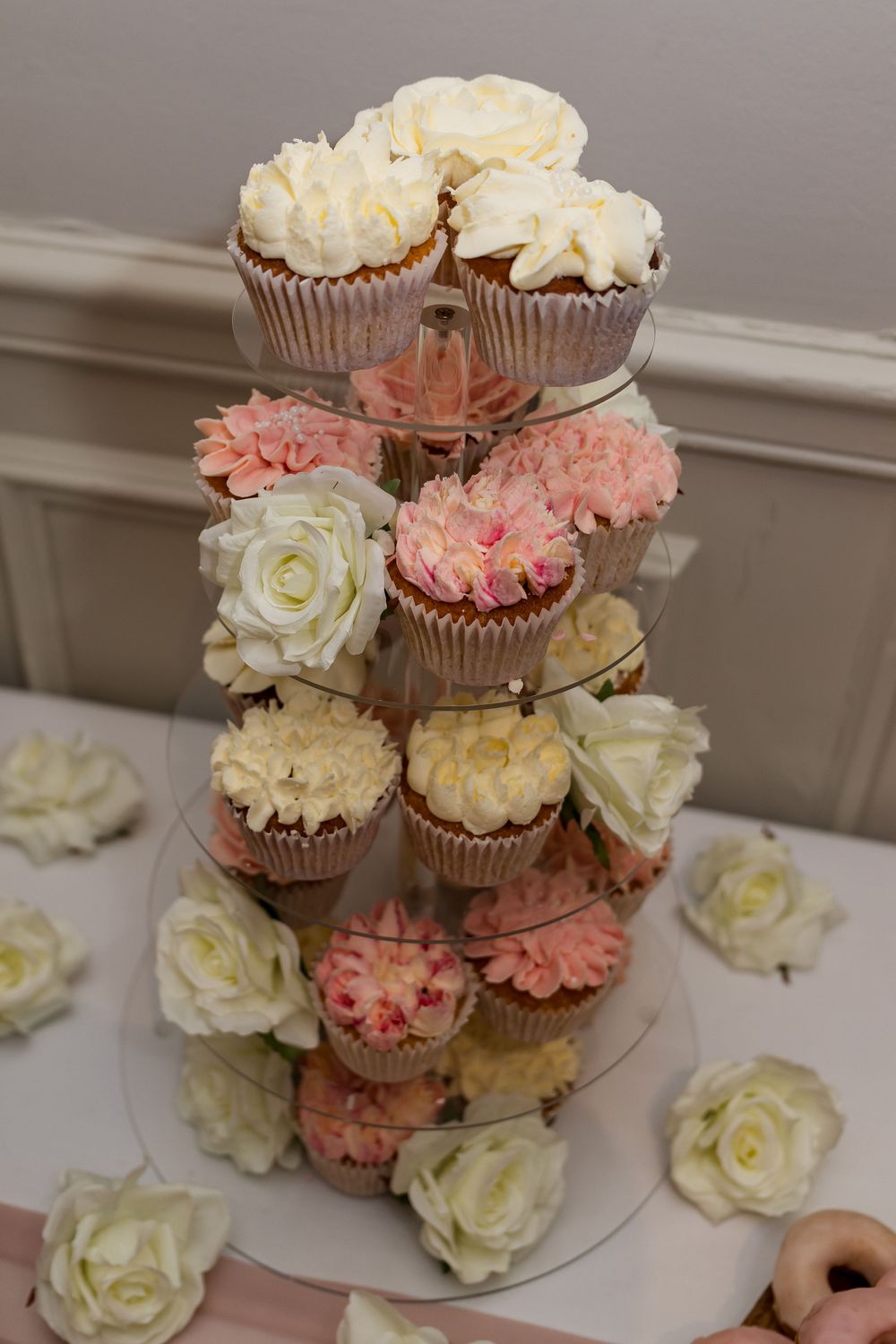 Elegant tiered cupcake tower with pink and white frosted cupcakes and fresh roses, perfect for weddings.