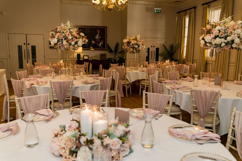 Elegant wedding reception hall with blush pink floral centerpieces, gold chiavari chairs, and candlelit round tables.