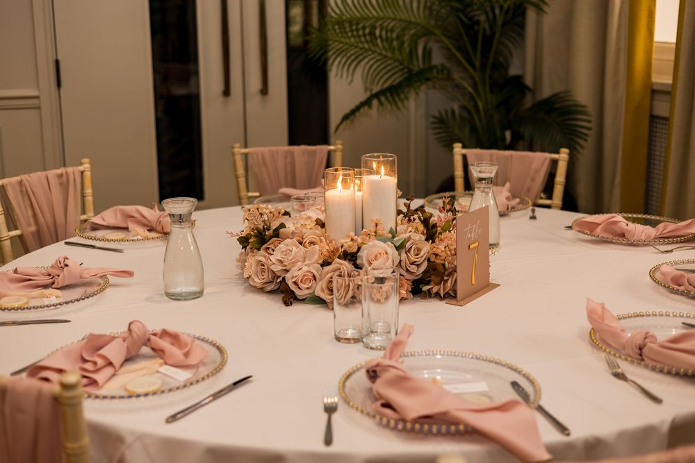 Elegant wedding reception table with pink roses centerpiece, candles, and blush pink napkins.