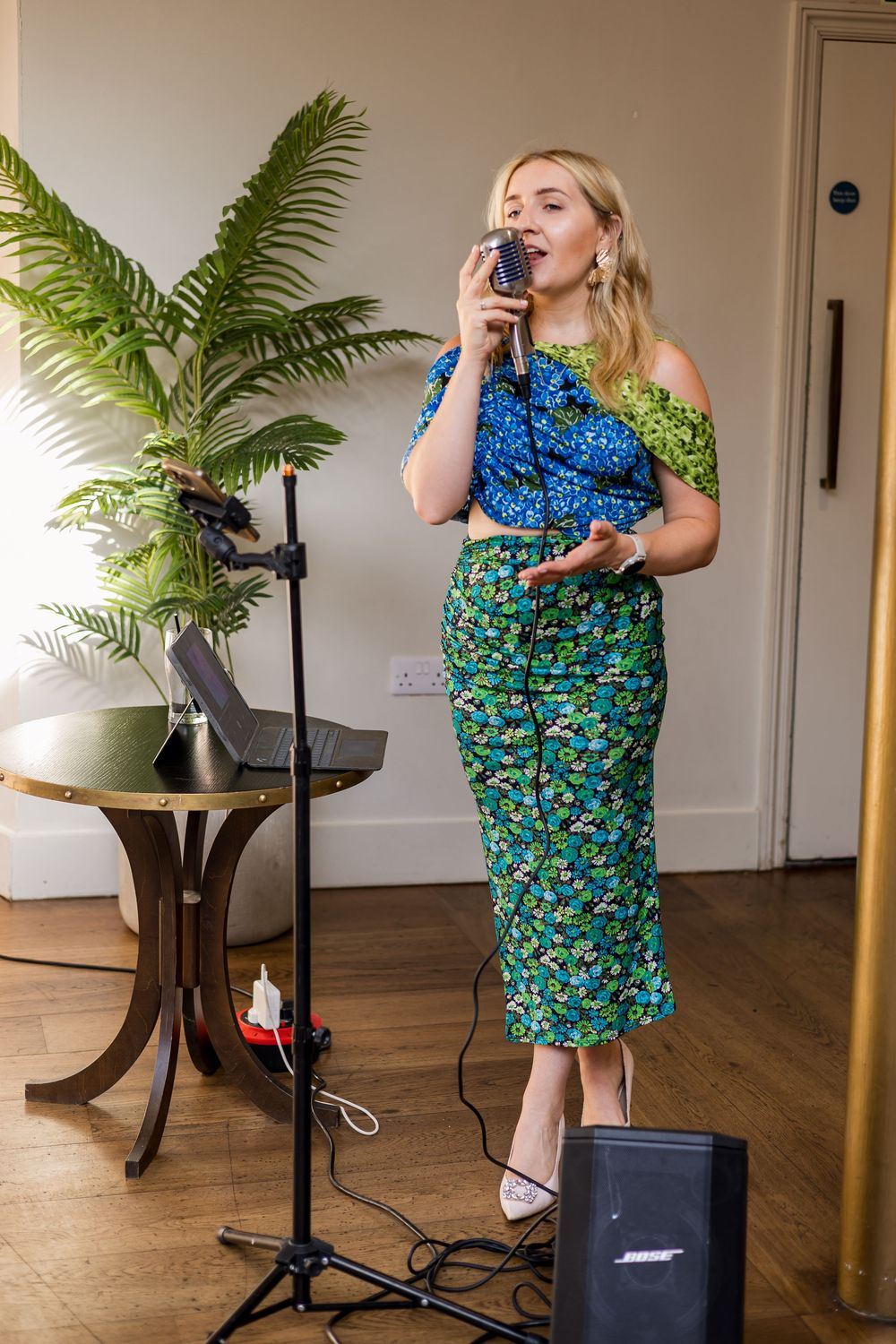 Female singer in floral outfit performs at wedding reception with vintage microphone.