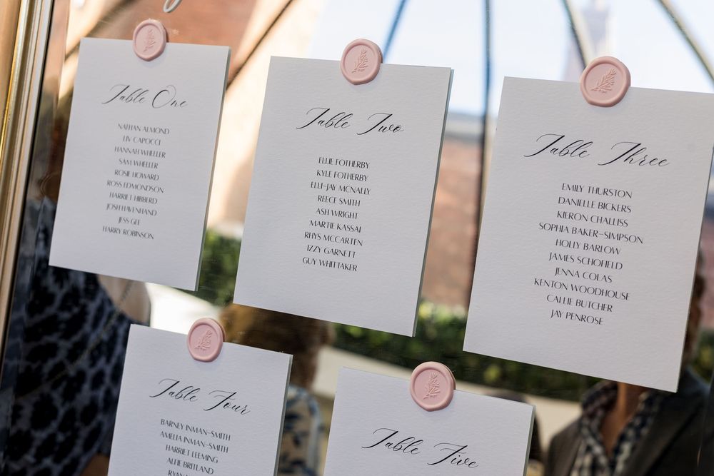 Elegant wedding seating chart cards with wax seals displayed on a glass surface.