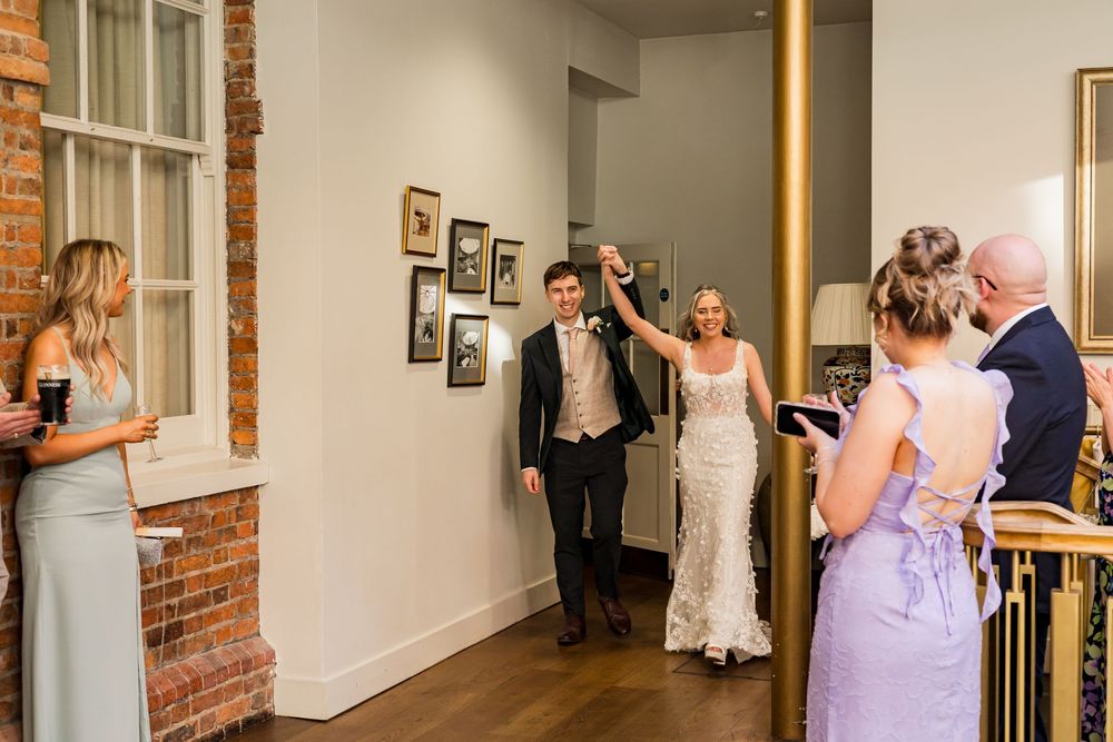 Newlywed couple makes grand entrance at wedding reception, greeted by smiling guests.