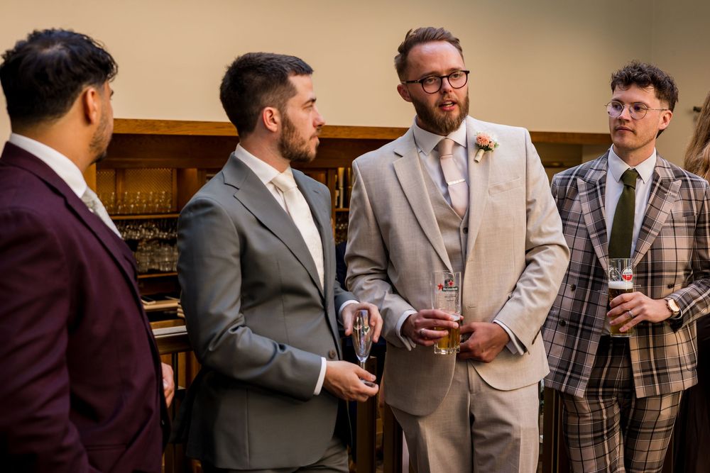 Groom in beige suit chats with groomsmen in varied suits at wedding reception.