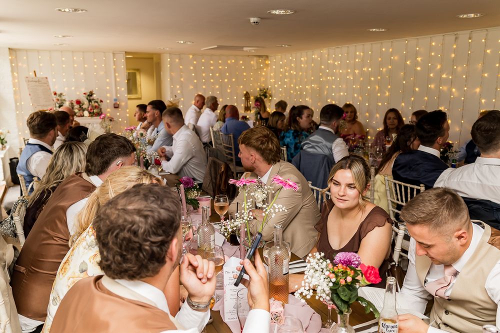 Guests celebrating at an elegant wedding reception with fairy lights backdrop and floral centerpieces.