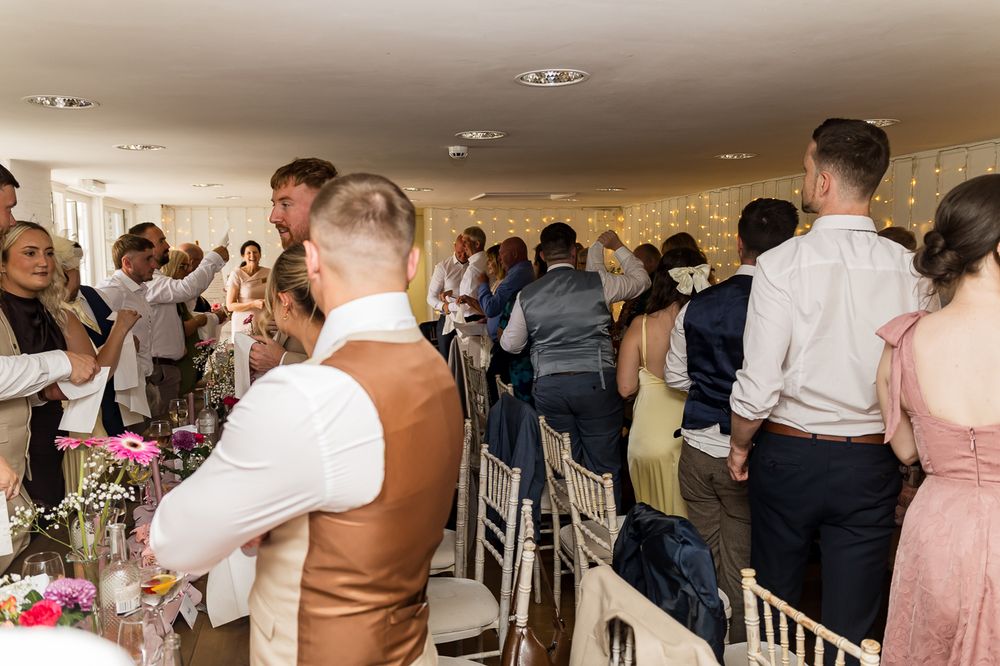 Guests standing and celebrating at an elegant wedding reception in a decorated venue with fairy lights.