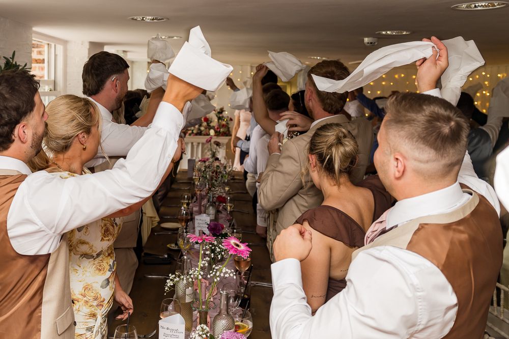 Wedding guests waving white napkins in celebration at a festive reception dinner table.