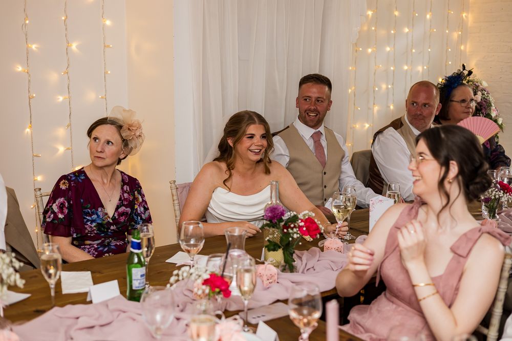 Wedding reception guests laughing and celebrating at elegantly decorated table with fairy lights and floral centerpieces.
