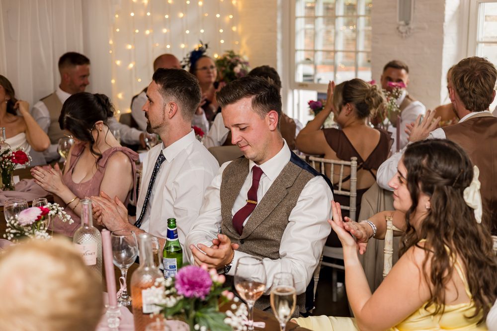 Guests applauding at a wedding reception in a decorated venue with fairy lights and floral centerpieces.