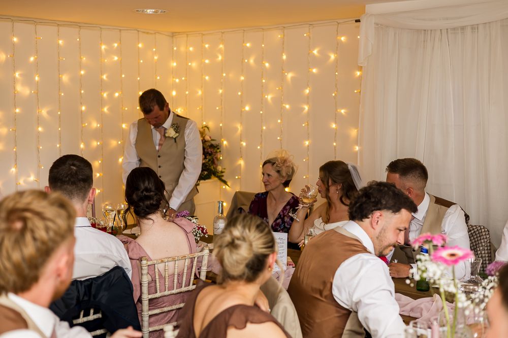 Guests gathered at elegant wedding reception with fairy light backdrop, bride and groom at head table with candles.