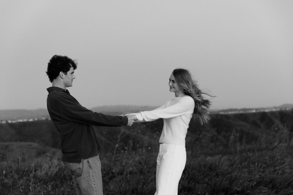 Black and white photo of a couple holding hands and dancing together outdoors in a field.